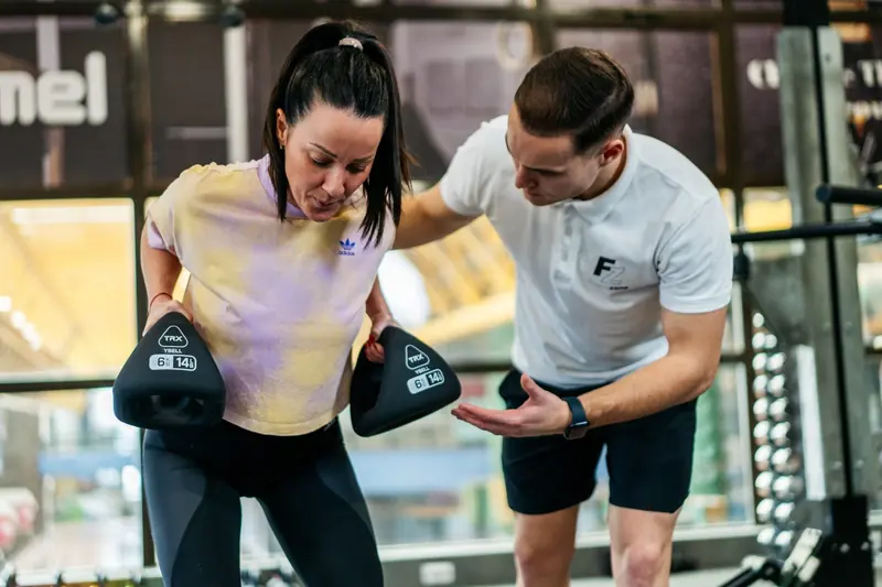 A trainer guiding a client through a functional exercise with boxing pads in a bright gym